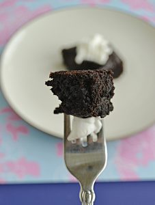 A close up of a piece of brownie of a fork with a plate in the background with a brownie on it.