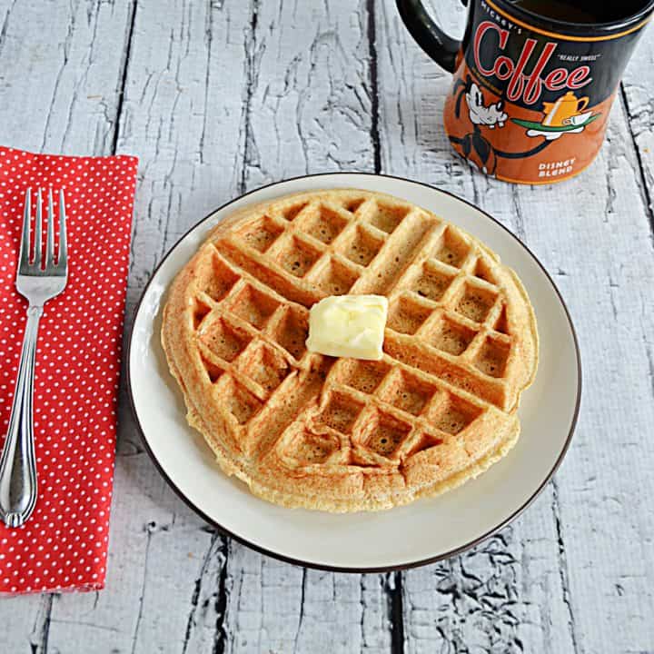 A close up of a plate with Apple Spice Cake Mix Waffle, a red napkin with a fork on it, and a Mickey Mouse mug of coffee.