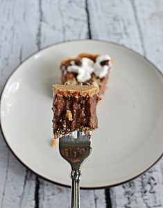 A fork with a bite of No Bake S'more Pudding Pie on it with a piece of the pie in the backgrounf.