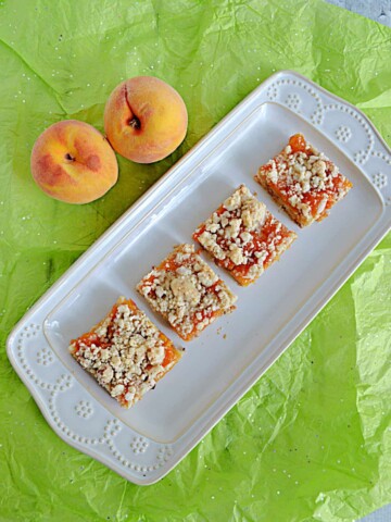 A platter with 4 Peach Pecan Bars on it and two peaches resting behind the platter.