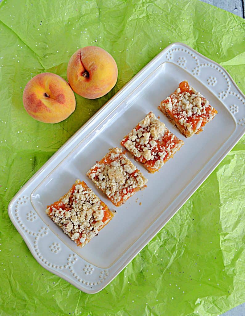 A platter with 4 Peach Pecan Bars on it and two peaches resting behind the platter.