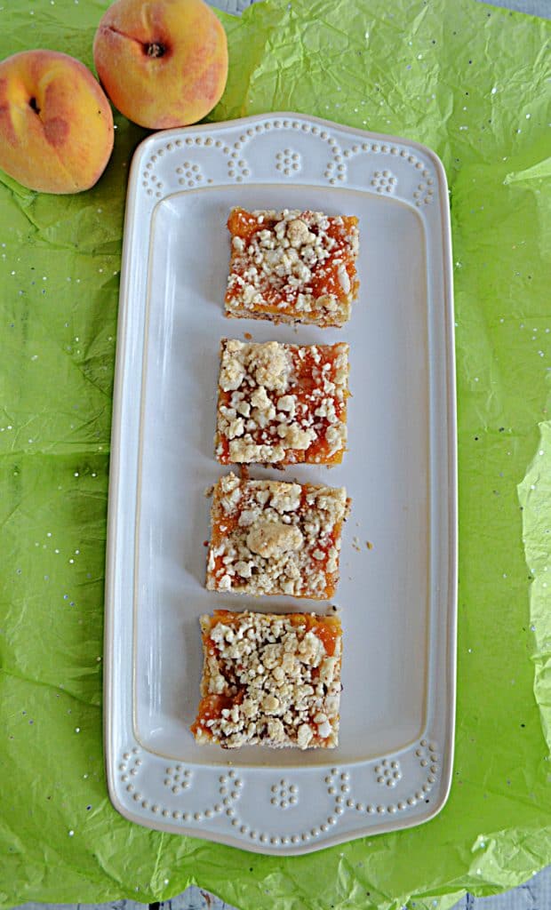 A platter with 4 Peach Pecan Bars on it and 2 peaches behind the platter.