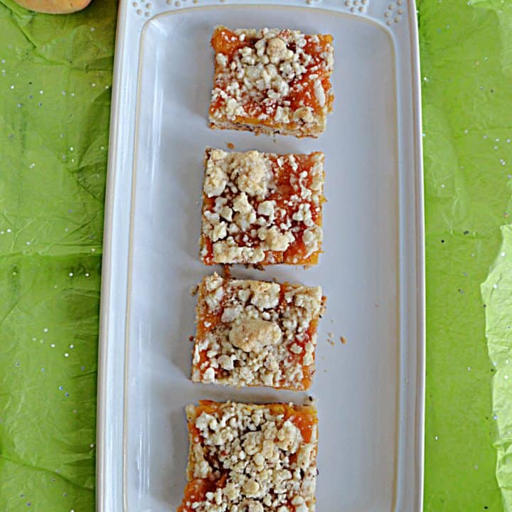 A platter with 4 Peach Pecan Bars on it and 2 peaches behind the platter.