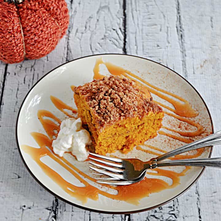 A plate with a caramel drizzle, two forks, and a slice of Pumpkin Spice Coffee Cake on it with a dollop of whipped cream next to it.