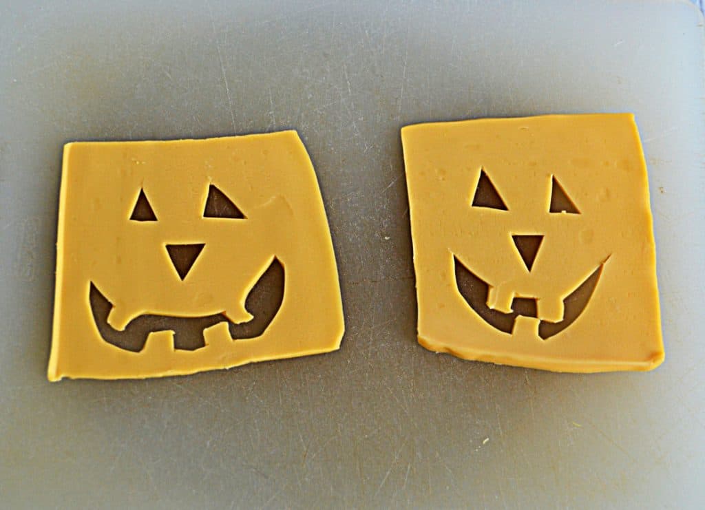Two slices of cheesse with Jack-o-lantern cut out faces on them. 