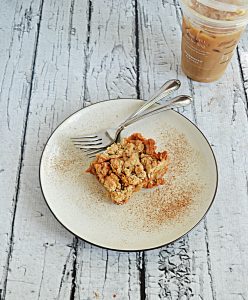 A plate with a Butterscotch Oat Bar with two forks and a cup of iced coffee in the background.