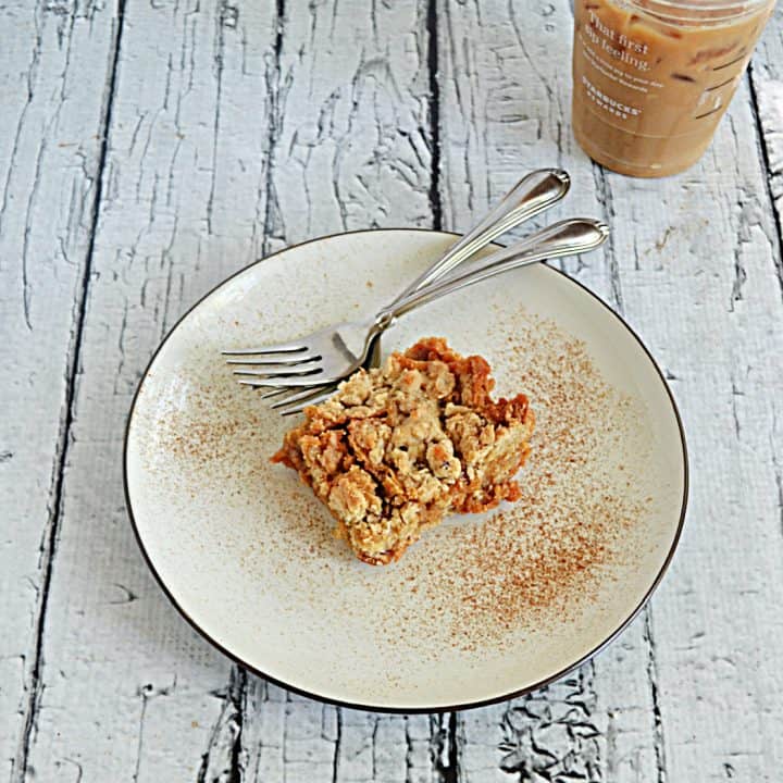 A plate with a Butterscotch Oat Bar with two forks and a cup of iced coffee in the background.