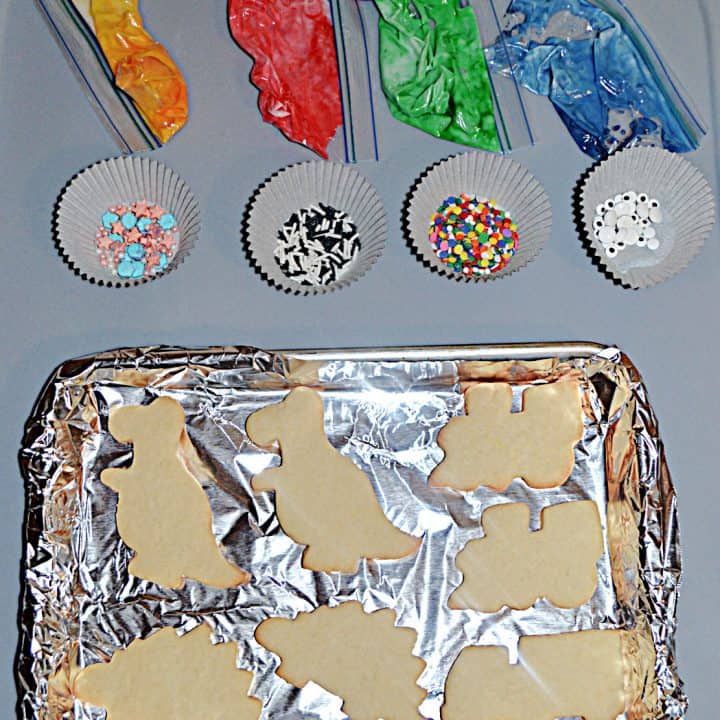 A sheet with cookies on it, 4 cups of sprinkles, and 4 bags of frosting.
