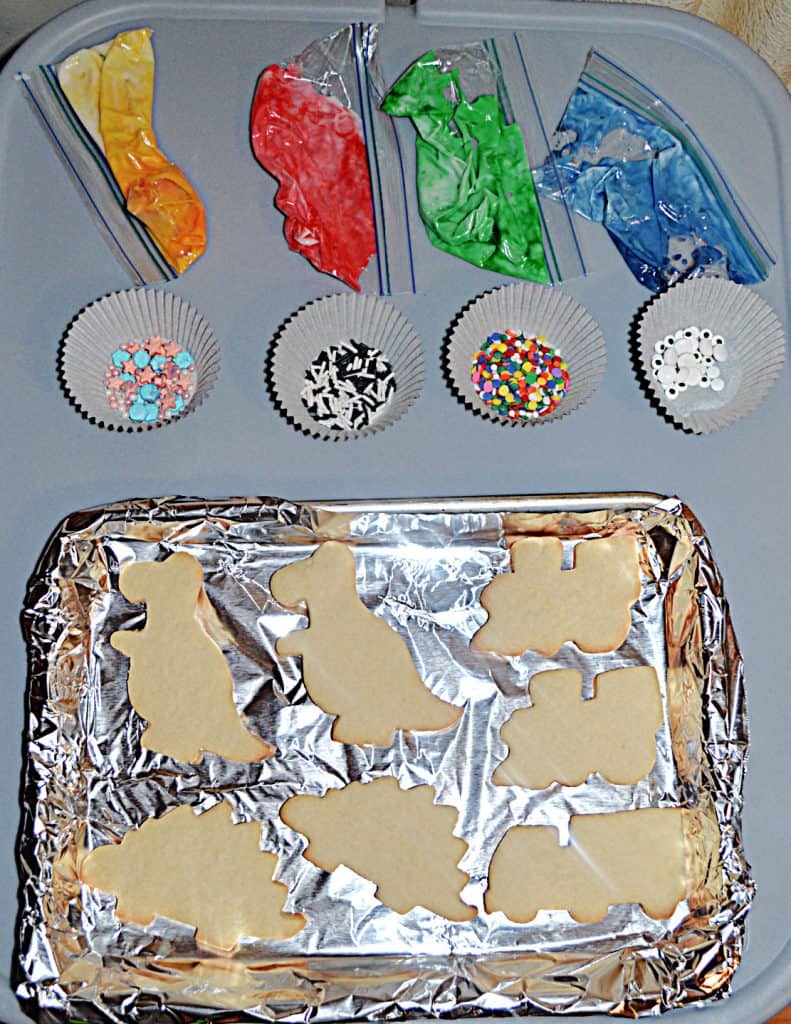 A sheet with cookies on it, 4 cups of sprinkles, and 4 bags of frosting. 