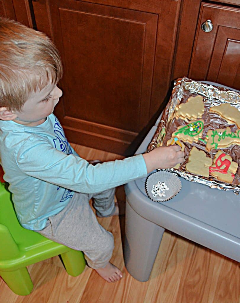 A toddler sitting at a table putting sprinkles on a pan of cookies.