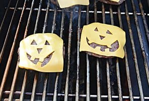Two burgers on a grill with jack-o-lantern cheese on top!