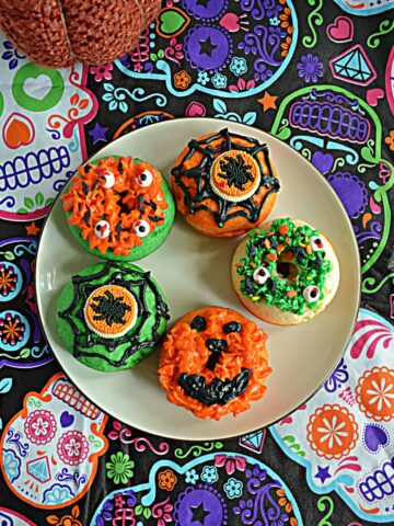 A plate with 5 orange and green Halloween Monster Donuts on it.