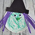 A paper plate witch colored green with google eyes and a nose and purple paper hair sstrips and a black hat.