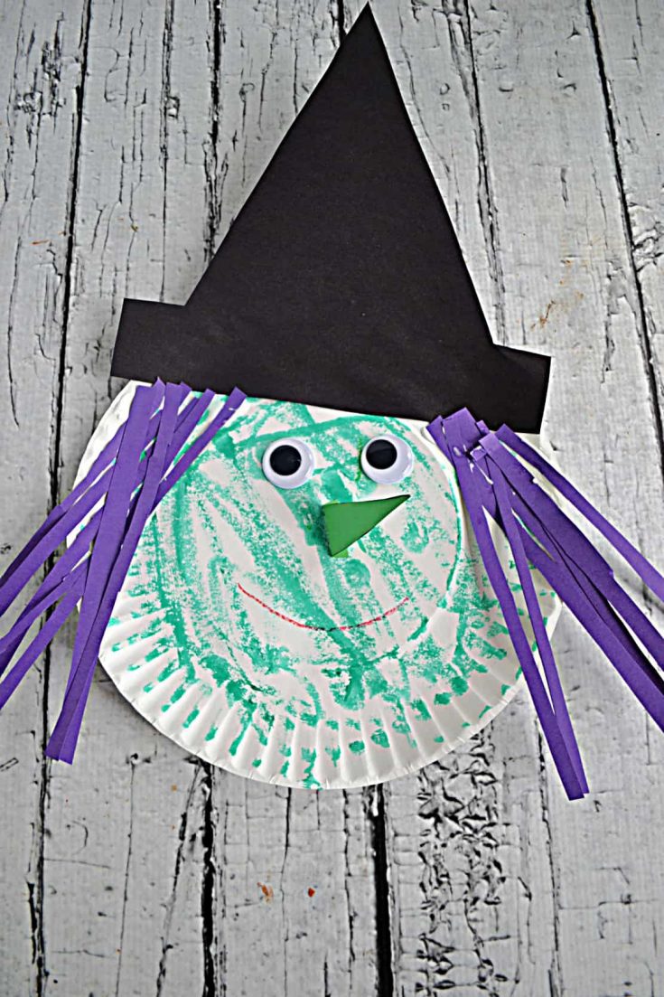 A paper plate witch colored green with google eyes and a nose and purple paper hair sstrips and a black hat.