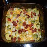 A glass baking dish filed with Brussels Sprouts in a cream cheese and cheddar mixture with crispy bacon on top.
