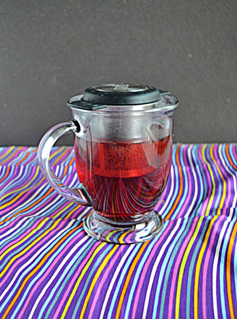 A mug of red tea with a tea infuser sitting it.