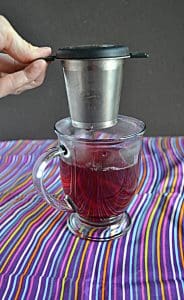 A hand pulling a tea infuser out of a ruby red mug of tea.