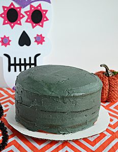 A layer cake topped with black buttercream and a skull decoration behind it.