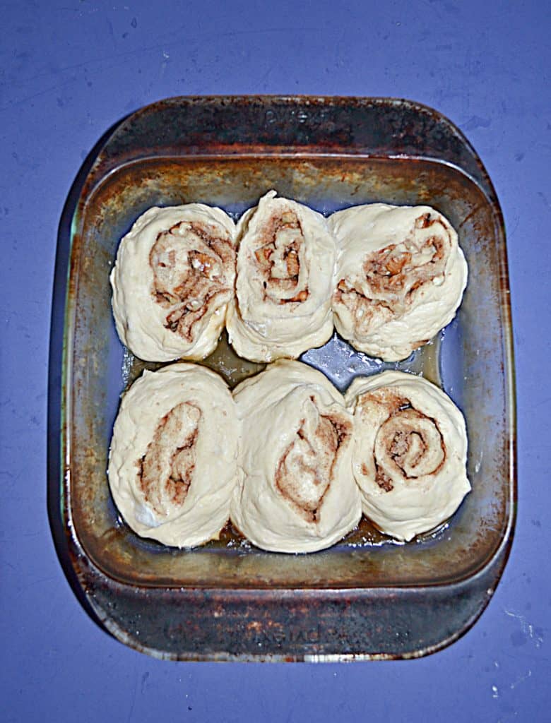 A baking dish with six unbaked cinnamon rolls in it. 
