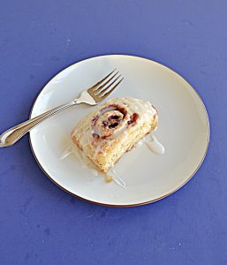 A plate with a cinnamon roll topped with vanilla icing and a fork on the plate.