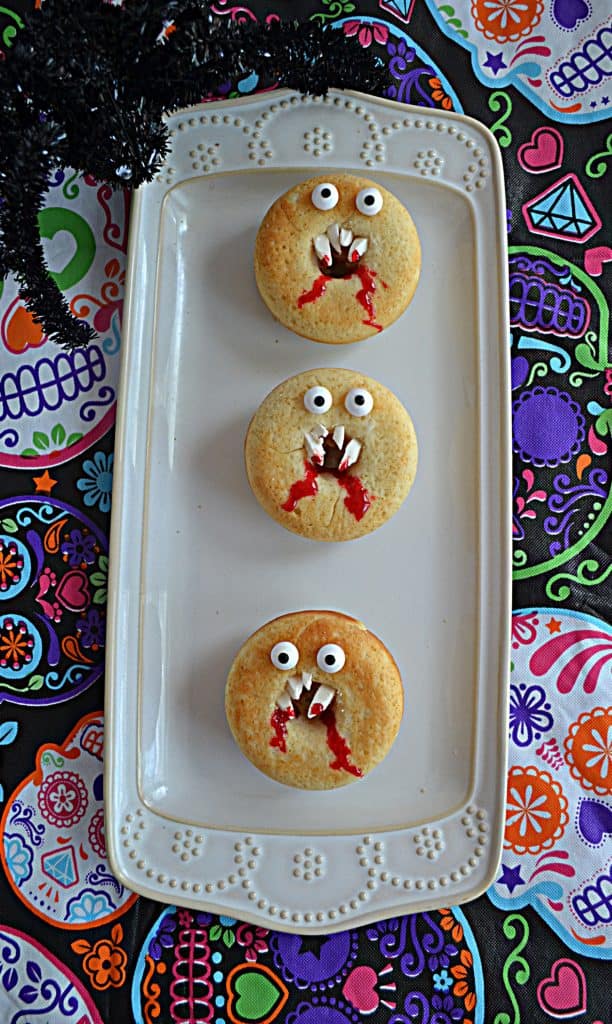 A platter with three vanilla donuts that look like vampire faces.