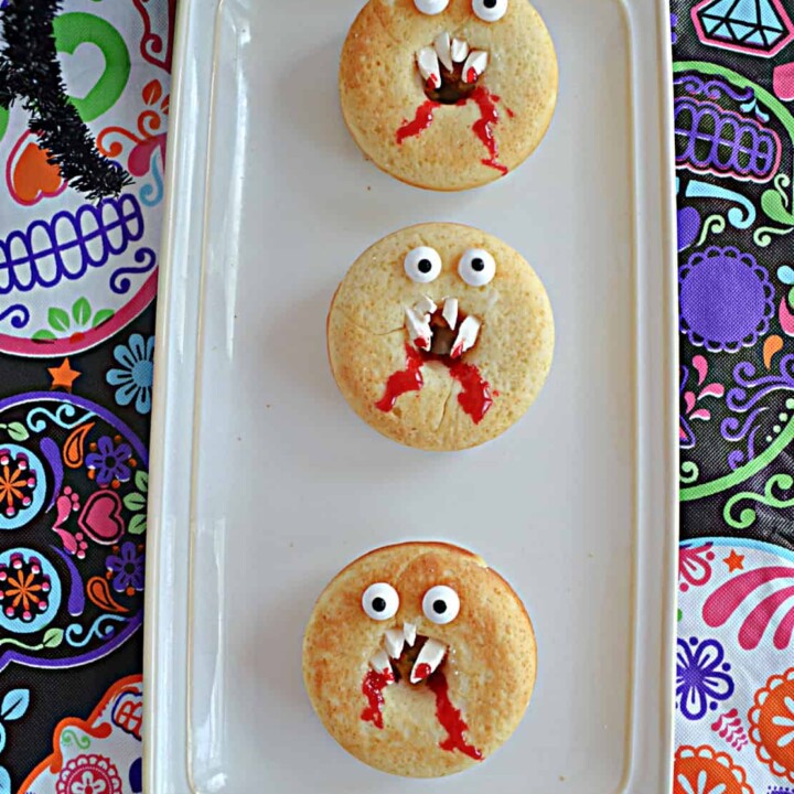 A platter with three vanilla donuts that look like vampire faces with fangs and edible eyes.