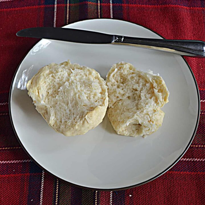 A plate with a dinner roll cut in half and a knife on top of the plate.