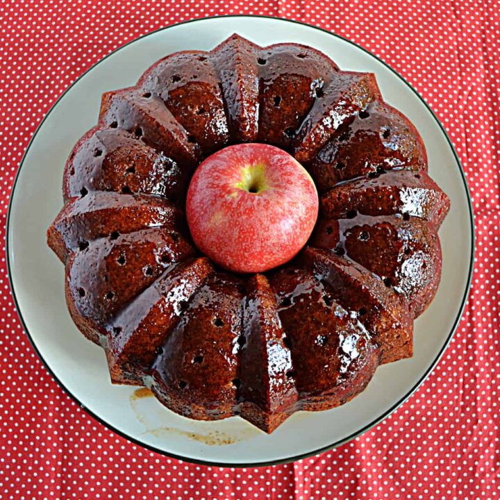 A plate with an Apple Cider Bundt Cake on it with an apple in the middle of the Bundt.