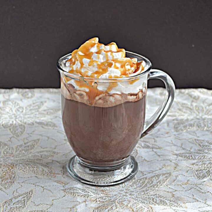 A mug of hot chocolate topped with whipped cream and drizzled with caramel sauce.