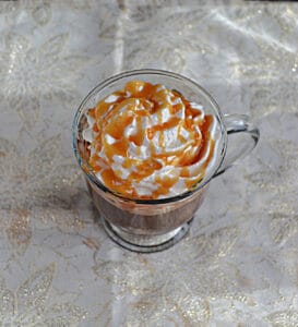 Top view of a mug of hot chocolate topped with whipped cream and caramel sauce.