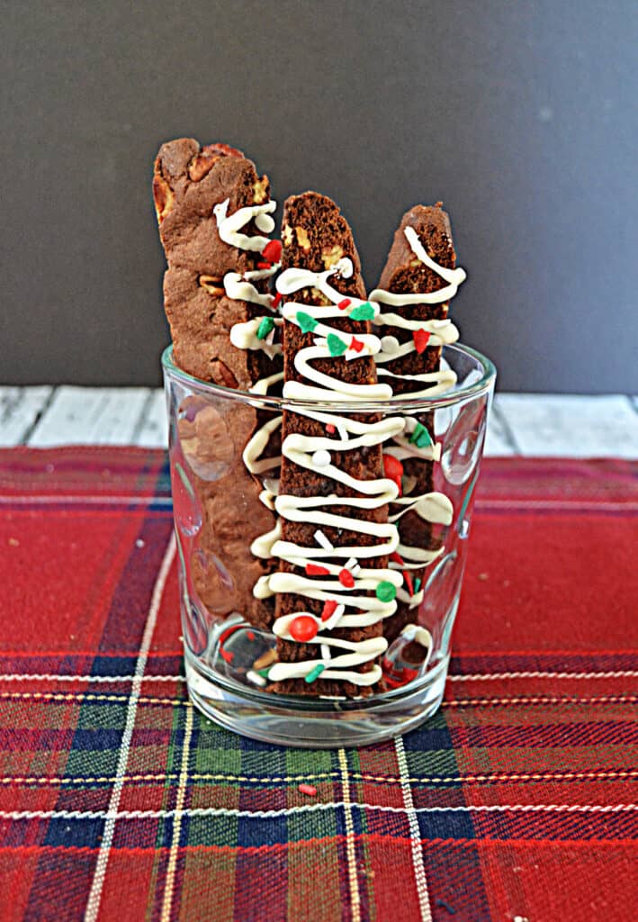 A glass with three chocolate biscotti drizzled with white chocolate.