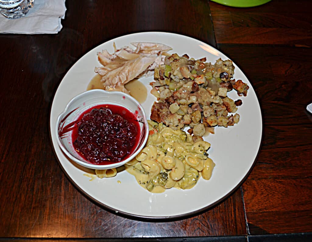 A plate filled with turkey, stuffing and gravy, cauliflower gratin, and a bowl of cranberry saucec. 