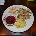 A plate filled with turkey, stuffing and gravy, cauliflower gratin, and a bowl of cranberry saucec.