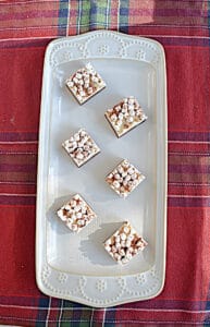 A white platter with six hot chocolate fudge squares topped with mini marshmallows arranged on it.