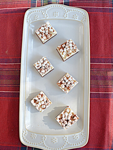 A white platter with six hot chocolate fudge squares topped with mini marshmallows arranged on it.