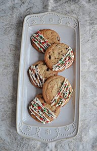 A white platter stacked with cookies drizzled in white chocolate and sprinkles.