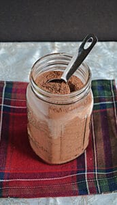 A jar of hot cocoa mix with a spoon in it.