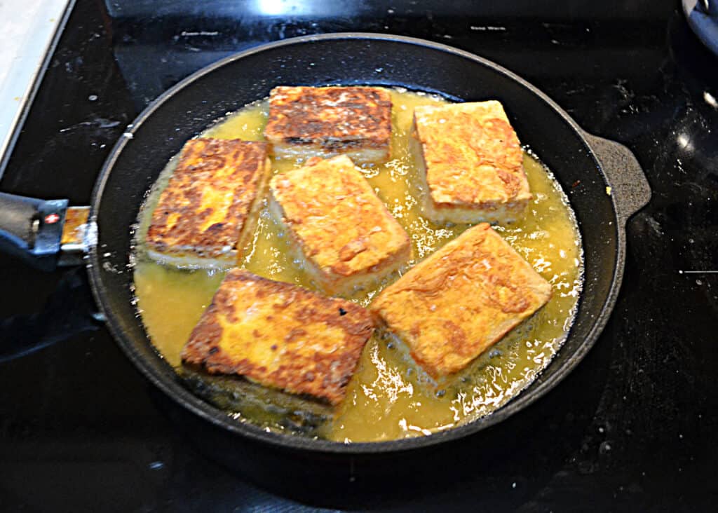 A skillet of tofu slabs frying in oil. 