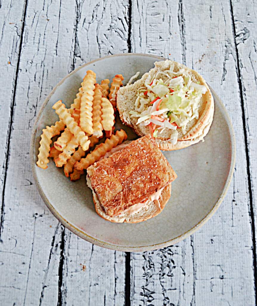A fried tofu slab on a bun with cabbage and a serving of crinkle fries on the side. 