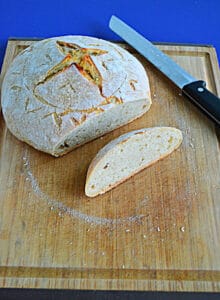 A close up view of a sourdough bread boule with a slice cut off and a serrated knife behind it.