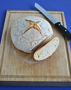A sourdough bread boule with a slice cut off and a serrated knife behind it.