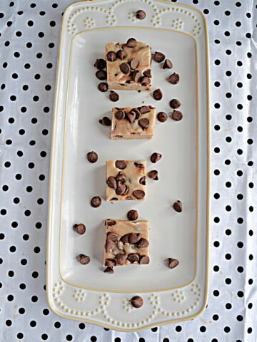 A white platter with squares of chocolate chip cookie dough fudge with chocolate chips sprinkled on top.