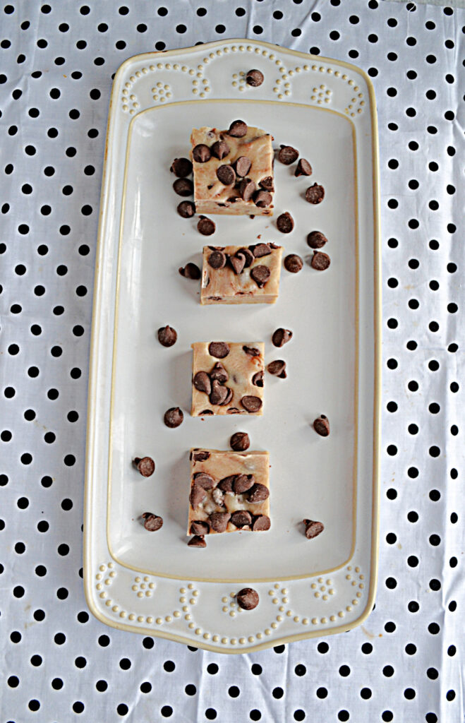 A white platter with squares of chocolate chip cookie dough fudge with chocolate chips sprinkled on top. 