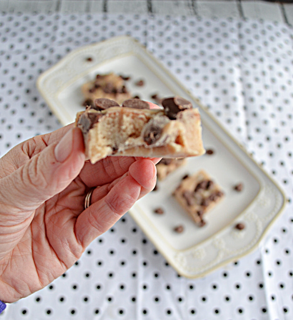 A close up view of a piece of chocolate chip cookie dough fudge with a bite taken out of it with a platter of cookie dough fudge in the background.