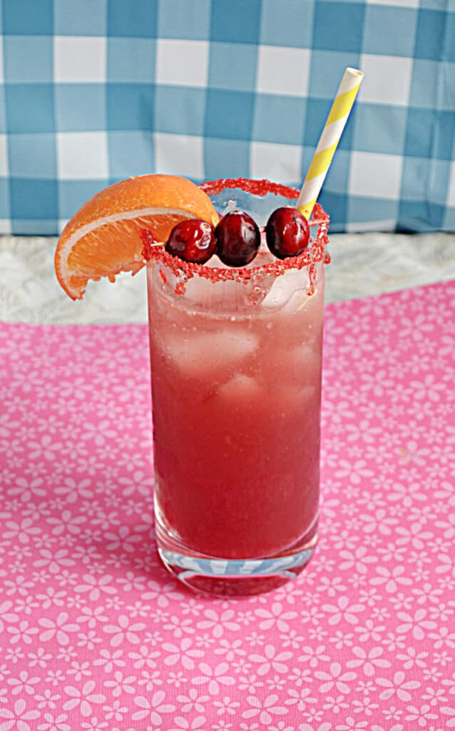 A glass filled with Cranberry Orange Mocktail with an orange wedge on the rim and three cranberries on top. 
