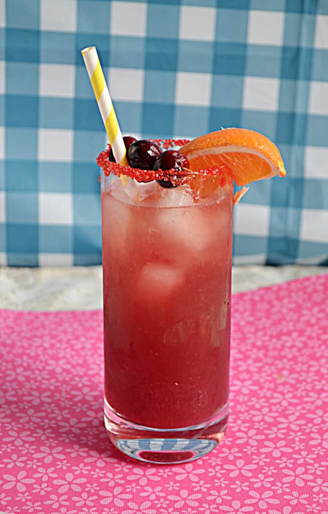 A glass of Cranberry Orange Spritzer with an orange wedge on the lip of the glass and cranberries on top. 