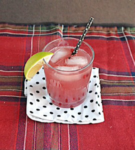 A glass of Pomegranate Moscow Mule with a lime wedge on the side and a straw.
