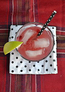 A top view of a Pomegranate Moscow Mule in a glass with ice, a lime wedge, and a straw.