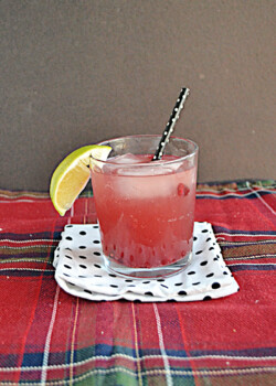 A Pomegranate Moscow Mule in a glass with ice, a straw, and a wedge of lime.