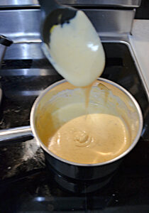 A pot of cheese sauce with a spoon over top of it dripping with the sauce.